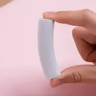 Silicone eyelash glue remover stick held between fingers on pink background, beauty skincare tool for eyelash extension removal, professional cosmetic accessory for lash care.