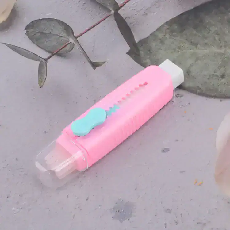 Shaving razor with pink handle and blue lubricating strip lying on concrete surface near green leaves, close-up image.