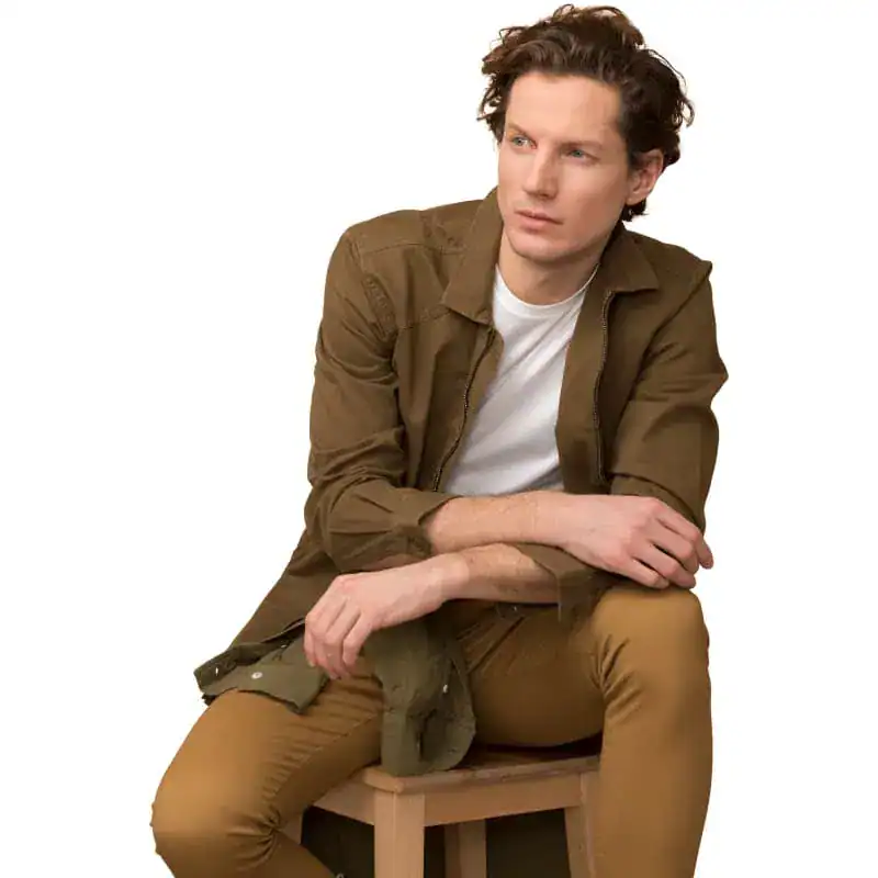 Elegant man in casual brown jacket and beige pants sitting on wooden stool, promoting stylish eyewear and optometry products at Monalisa Store.