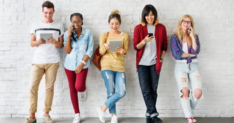 Teenage group of diverse friends using smartphones and tablets against a white brick wall at Monalisa Store opt center.