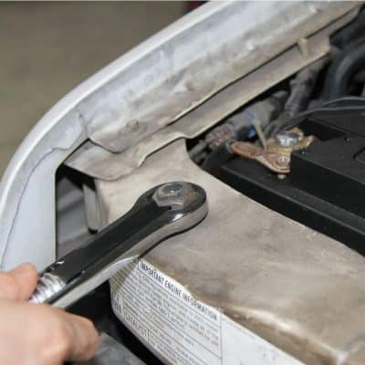 Close-up of hand using a wrench on a car engine for maintenance and repair.