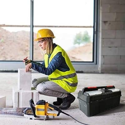 Detailed description of a female construction worker wearing a safety helmet and high-visibility vest working on bricks with tools at a building site.