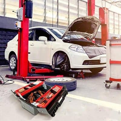 A white sedan car on a hydraulic lift at an auto repair shop with the hood open, tools and spare tire nearby, indicating a vehicle maintenance or repair task underway.