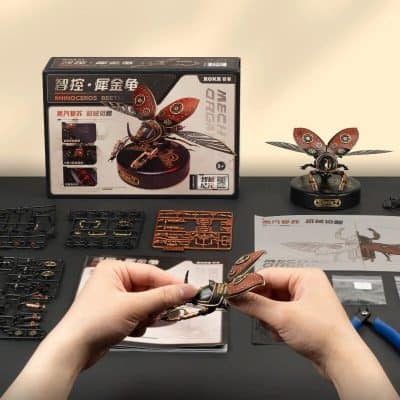 Detailed image of a mechanical rhinoceros beetle model kit for assembly, featuring parts and tools on a workspace, showcasing DIY insect figurine, perfect for educational and hobbyist use.