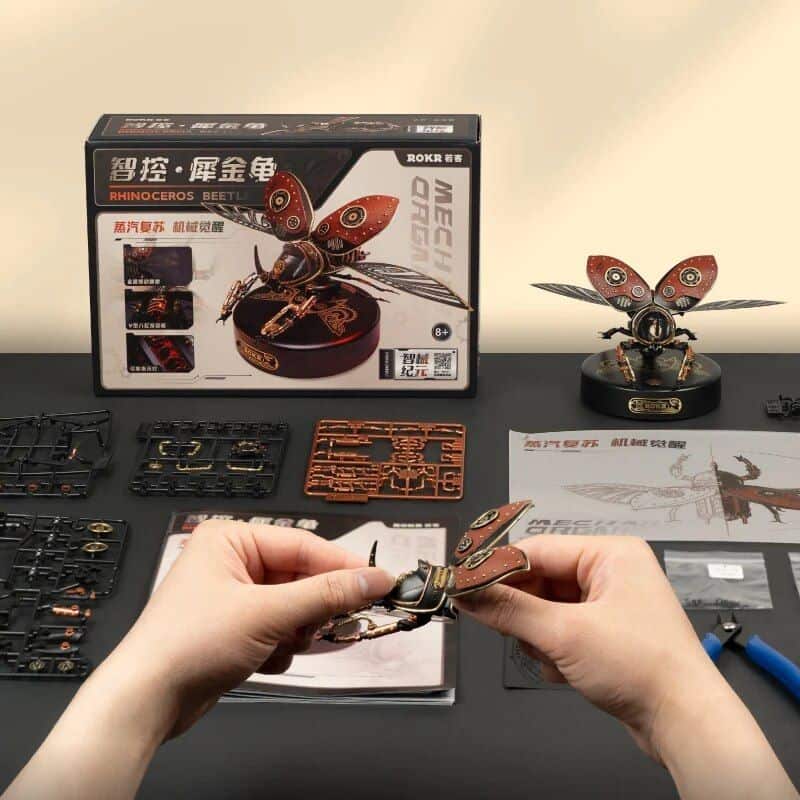 Detailed image of a mechanical rhinoceros beetle model kit for assembly, featuring parts and tools on a workspace, showcasing DIY insect figurine, perfect for educational and hobbyist use.