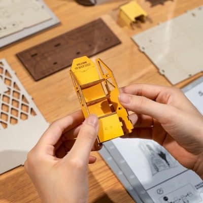Detailed image of a small, yellow dollhouse shelf being assembled, showcasing mini furniture pieces, perfect for hobbyists and collectors.