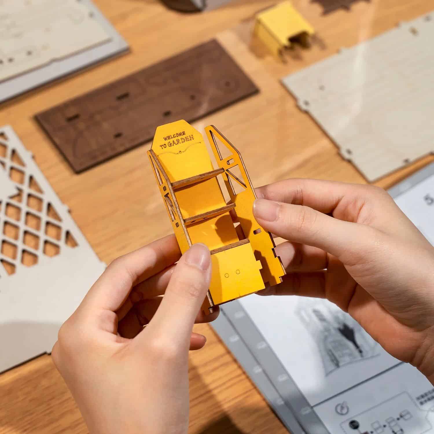 Detailed image of a small, yellow dollhouse shelf being assembled, showcasing mini furniture pieces, perfect for hobbyists and collectors.