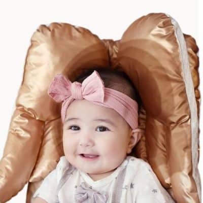 Adorable baby girl with a pink headband and bow, seated in a plush, satin-like baby chair. Perfect for baby care accessories, baby chairs, and infant comfort products.