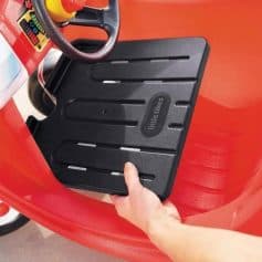 Alt text: Child's hand pressing the black plastic pedal of a ride-on toy car with a red body and steering wheel.