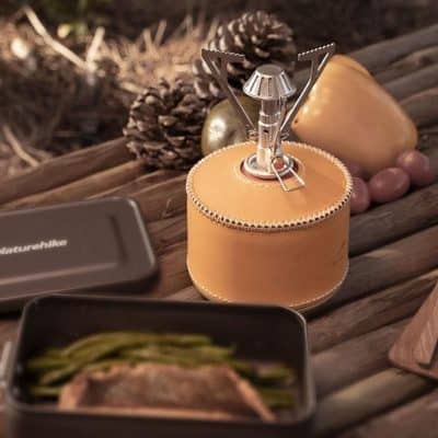 Portable camping stove and optical gear on wooden table with pinecones and natural decor.