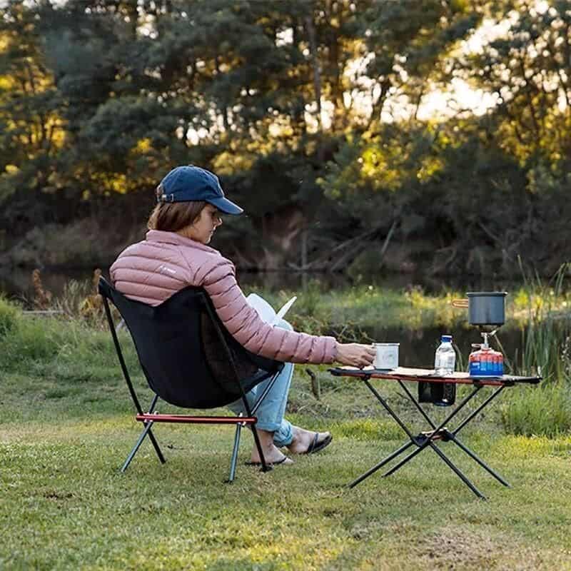 Relaxing woman reading outdoors by a lake, enjoying nature with camping gear, perfect for outdoor leisure and camping accessories.
