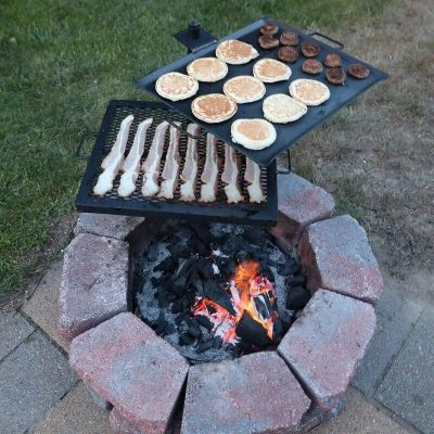 Delicious breakfast foods grilling over an open flame on a backyard fire pit, featuring pancakes, bacon, and sausage. Perfect outdoor cooking setup for a casual family meal.