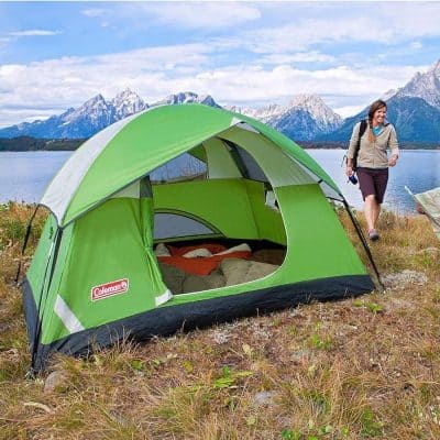 Bright green Coleman camping tent on lakeside with mountains in background, perfect for outdoor activities and nature outdoor trips.