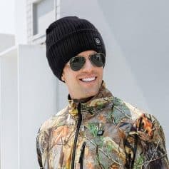 Stylish black beanie hat with logo, perfect for cold weather, paired with sunglasses and outdoor camo jacket, showcasing trendy winter fashion.