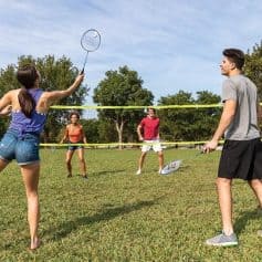 A group of young adults playing badminton on a sunny day in a park, enjoying outdoor sports and recreational activities.