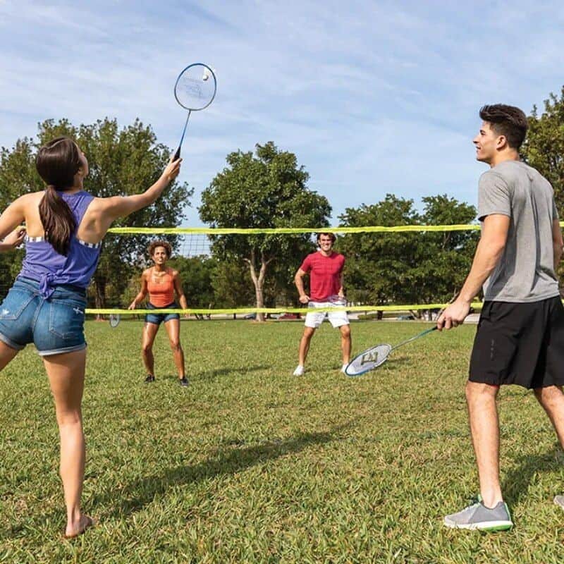A group of young adults playing badminton on a sunny day in a park, enjoying outdoor sports and recreational activities.