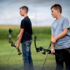 Young boys practicing archery outdoors, focusing on target shooting, sport accessories, and proper gear in a natural setting.