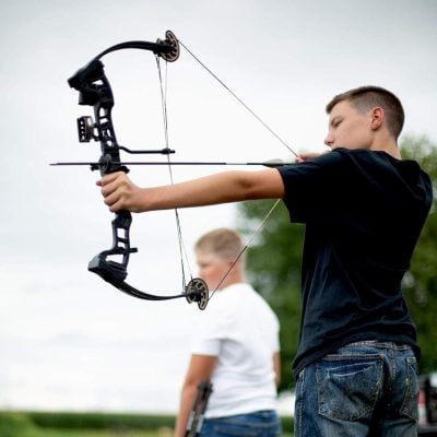 Young man aiming with a compound bow at an outdoor archery range.
