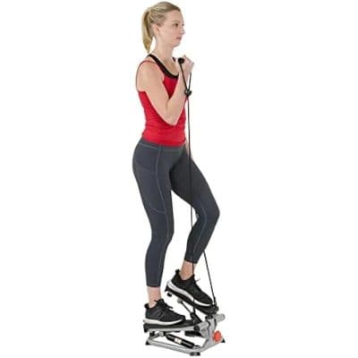 Healthy woman using a stepper for cardio workout, wearing athletic clothing, indoors exercise on compact fitness machine for weight loss, fitness, and cardiovascular health.