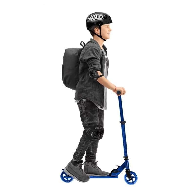 Child with helmet riding a scooter, wearing knee and elbow pads, backpack, and casual outfit, white background.