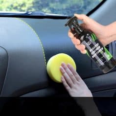 Alt text: Person applying plastic leather restorer spray and cleaning car dashboard with a yellow sponge to maintain vehicle interior quality.