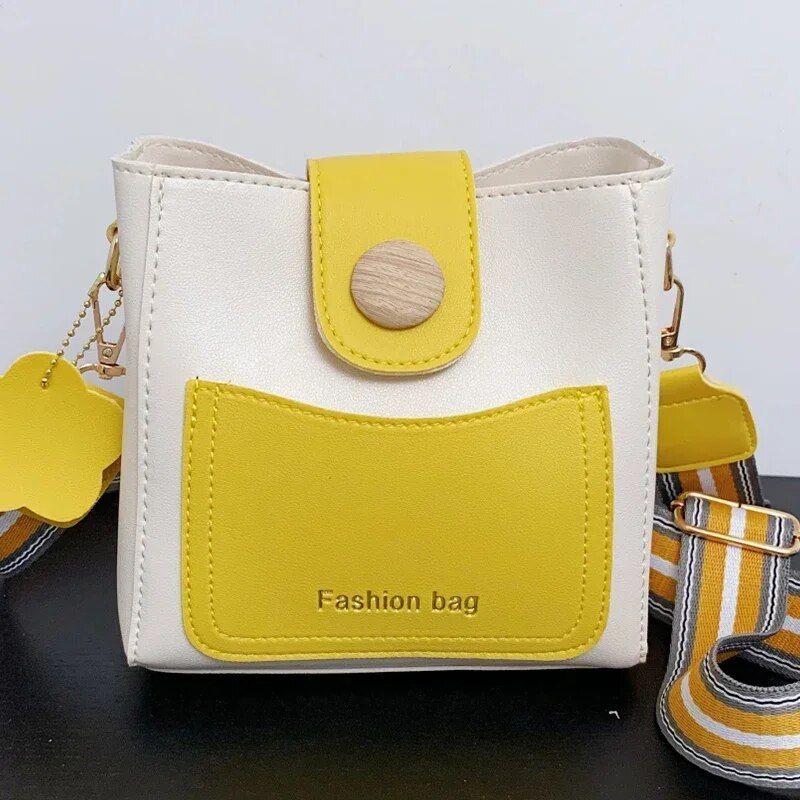 Bright yellow and white fashion handbag with adjustable striped strap, front pocket, and wooden button closure, perfect for stylish accessories.