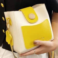 Stylish yellow and white fashion bag with front pocket, button clasp, and decorative charms, ideal for trendy accessories and everyday use.