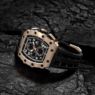 A high-end men's luxury chronograph watch with a black dial, multiple sub-dials, and a square gold-tone case, featuring a black rubber strap, displayed on a dark textured surface.