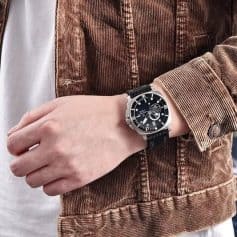 Stylish black watch on person's wrist with a brown corduroy jacket, showcasing trendy accessories at Monalisa Store. Perfect for fashion-conscious individuals seeking quality timepieces.