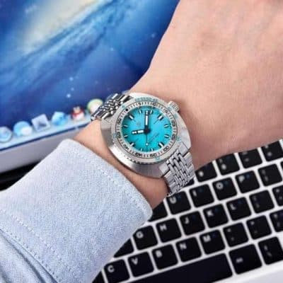 A person wearing a sleek silver watch with a bright blue face, showcased on the wrist with a background of a laptop keyboard, emphasizing luxury, style, and precision in watch design from Monalisa Store.