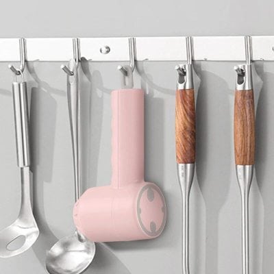 Modern pink silicone utensil holder hanging on a kitchen wall rack with stainless steel and wooden-handled tools.