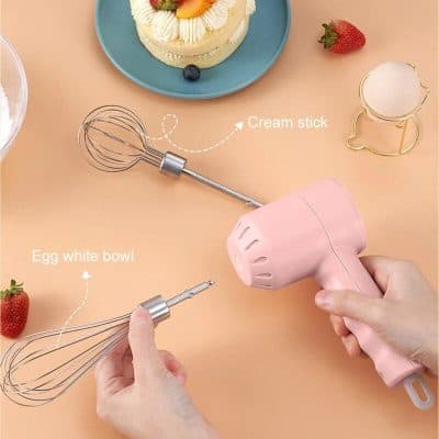An electric hand mixer with stainless steel beaters and creative labels on a pink background, perfect for baking enthusiasts.