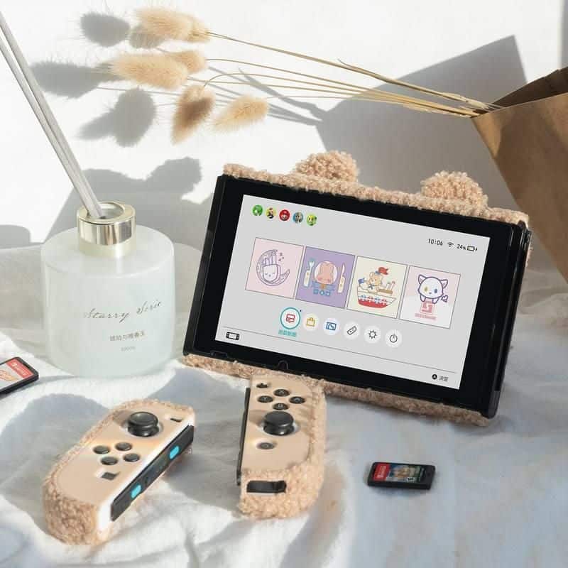 Cute gaming controllers with plush covers next to a tablet on a soft white surface.