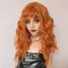 Close-up of a young woman with bright orange, wavy hair styled in layers, wearing bold makeup, dark lipstick, and eye-catching jewelry, showcasing trendy wig options at Mona Lisa Store.