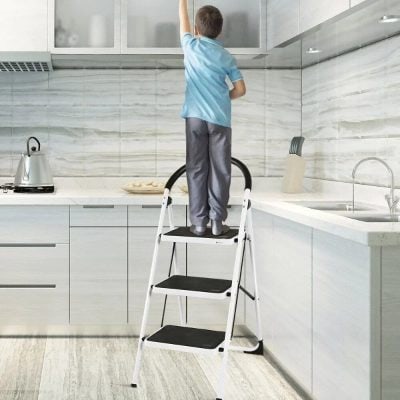 Child standing on a black and white step ladder in a modern kitchen.
