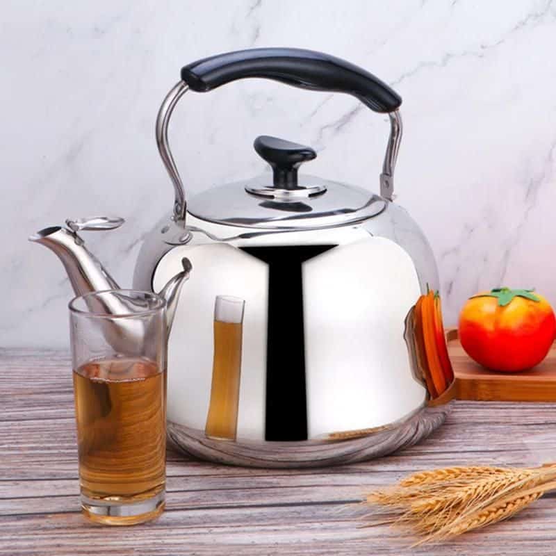 Elegant stainless steel teapot with black handle, glass of brewed tea, fresh apple, and sliced carrots on wooden table, ready for a healthy meal or tea break at Monalisa Store, promoting quality kitchen and dining essentials.