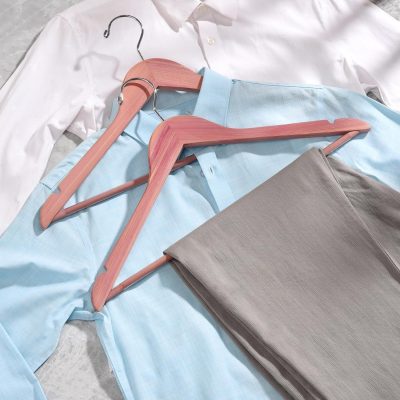 Alt text: Stylish clothing on pink wooden hangers featuring shirts and pants, perfect for fashion and clothing store display or wardrobe organization.