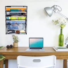 Bright workspace featuring a laptop, wall-mounted magazine rack, and decorative plants for a productive and organized office environment.