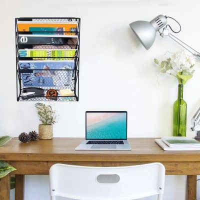 Bright workspace featuring a laptop, wall-mounted magazine rack, and decorative plants for a productive and organized office environment.