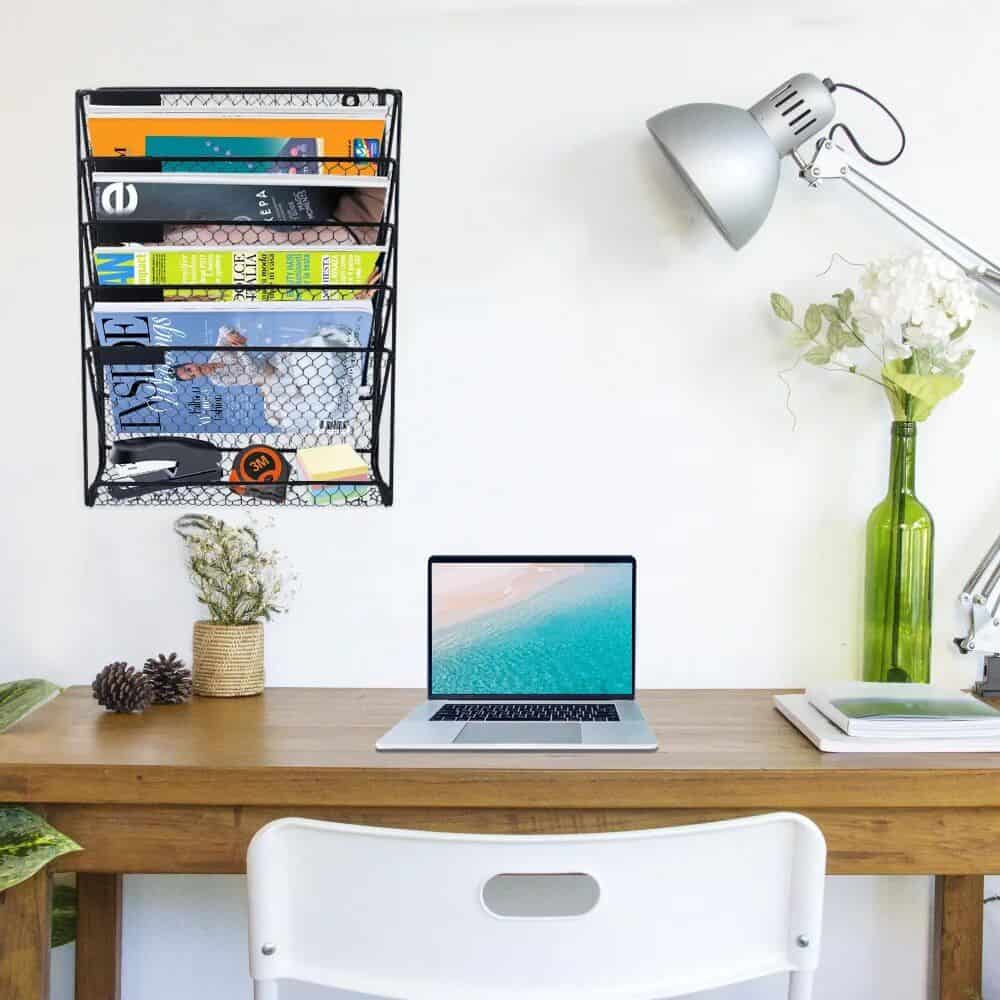 Bright workspace featuring a laptop, wall-mounted magazine rack, and decorative plants for a productive and organized office environment.
