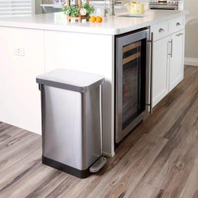 Stainless steel pedal trash can next to white kitchen cabinets and wine fridge, ideal for home or office use, combining durability, style, and functionality.