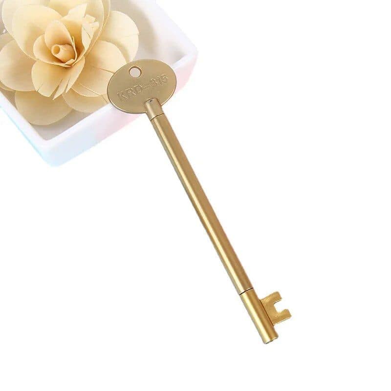 A gold-colored antique-style key resting beside a white flower in a small container. Perfect for vintage door decor or as a decorative key. Elegant and timeless design for home or office.