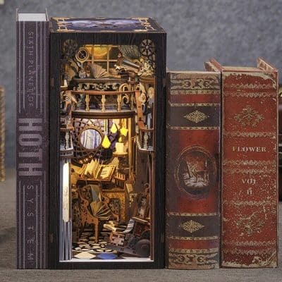 A miniature library scene inside a decorative box with tiny books, lamps, and furniture, surrounded by vintage book covers. Perfect for home decor, collectibles, and unique gift ideas.