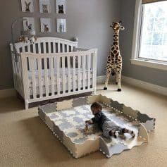 Baby playing on soft foam puzzle mat in a well-lit, cozy bedroom with animal-themed decor and a large window.