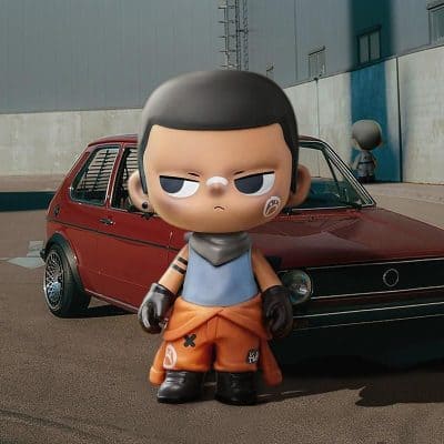 Cute stylized toy figure of a street racer with a rebellious look, standing in front of a red vintage car outside an industrial building.