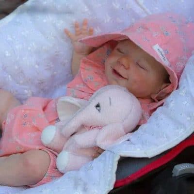 Cute baby girl in pink clothes with plush elephant toy, smiling and lying on a soft white blanket, ideal for kids and baby products.
