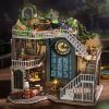 Detailed miniature dollhouse with clock tower, featuring stairs, books, and greenery, perfect for collector’s decor and opt enthusiasts seeking unique home accents.