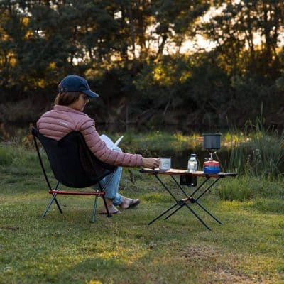 Enjoy a peaceful outdoor moment with a portable camping stove, coffee, and reading in nature at Monalisa Store, perfect for outdoor enthusiasts.