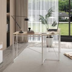 Minimalist office desk setup with laptop, desk lamp, books, and a large potted plant featuring tropical leaves, near a window with outdoor view, creating a bright and inspiring workspace for productivity.