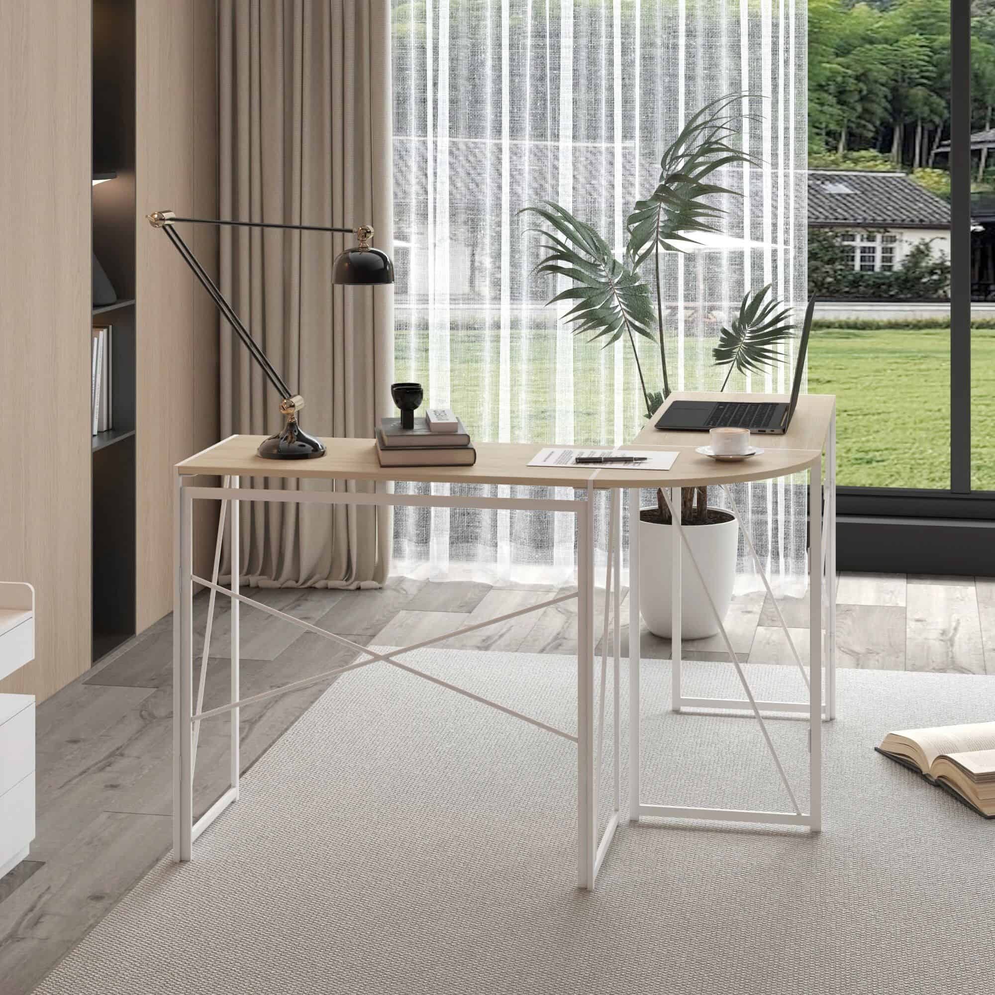 Minimalist office desk setup with laptop, desk lamp, books, and a large potted plant featuring tropical leaves, near a window with outdoor view, creating a bright and inspiring workspace for productivity.